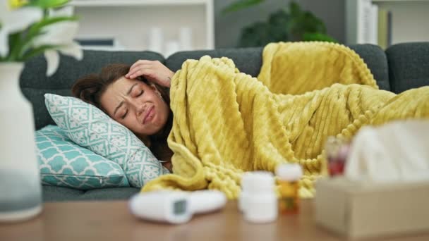 Młoda piękna Latynoska leżąca na kanapie chora temperatura pomiaru w domu - Materiał filmowy, wideo
