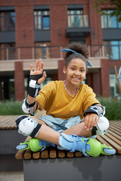 Portrait of African American roller girl sitting on bench outdoors and smiling at camera - Photo, Image