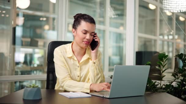 Oficinista latina ocupada multitarea, haciendo una llamada de cliente en su escritorio - Imágenes, Vídeo