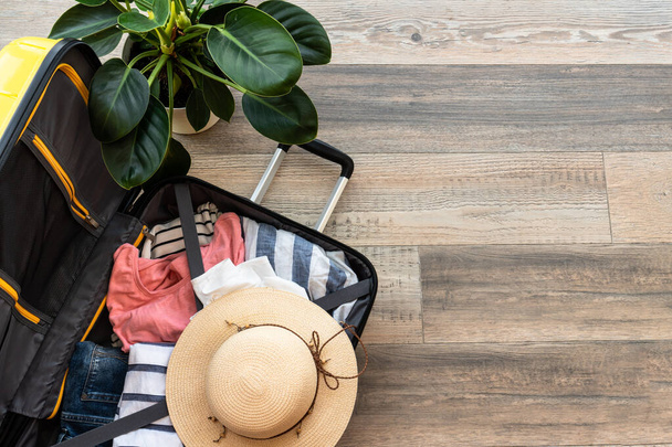 Nyílt bőrönd nyári ruhával, sapkával és útlevéllel. Utazási koncepció, csomagolás. Lapos feküdt kép fa háttér. - Fotó, kép