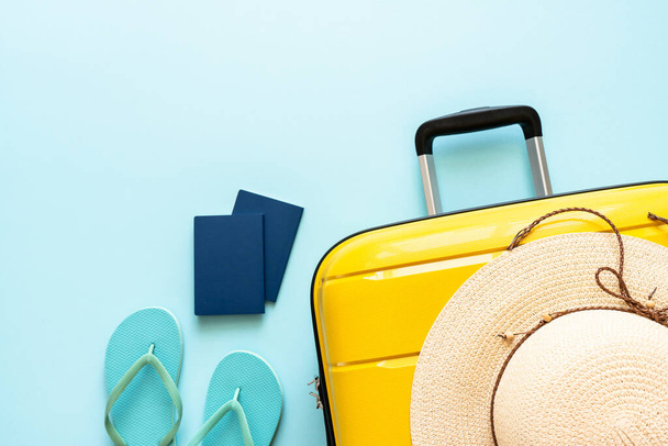 Koffer, Hut, Pässe und Flip-Flops auf blauem Hintergrund. Frohe Feiertage, Reisekonzept. Flaches Laienbild. - Foto, Bild