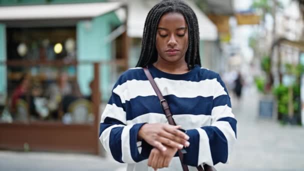Afričanky americká žena při pohledu na hodinky čeká s vážným výrazem na kavárně terasa - Záběry, video