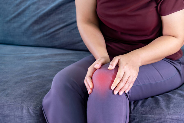Woman holding the knee with pain on sofa in living room at home. Old age. she is having symptoms Pain on both sides of the knee, due to osteoporosis, to retirement age and health care concept. - Photo, Image