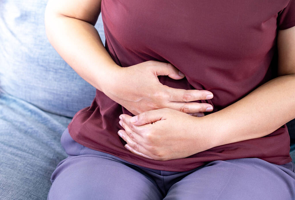 痛みを伴う胃痛を抱えている脂肪の女性. リビングルームのソファーの重量をコントロールしたいため,時間通りに食べる,慢性胃炎. 胃や月経クランプ。 体内の健康問題の炎症 - 写真・画像