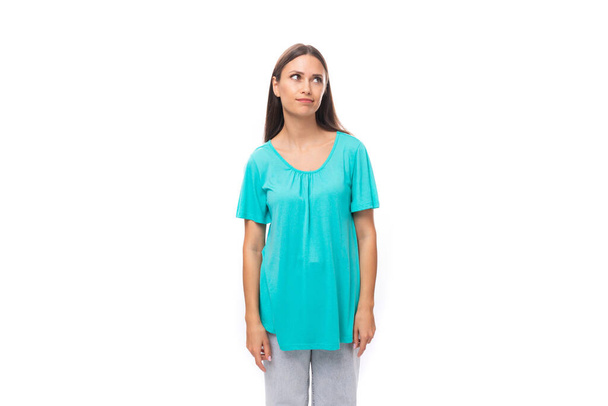 portret van een mooie jonge Kaukasische brunette vrouw met lang haar in een blauw t-shirt op een witte achtergrond met kopieerruimte. - Foto, afbeelding