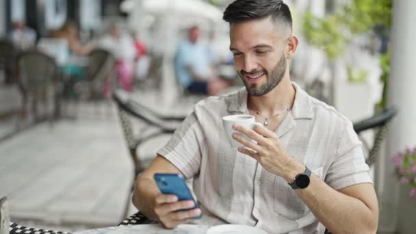 Joven hispano usando smartphone bebiendo café en la terraza de la cafetería - Metraje, vídeo
