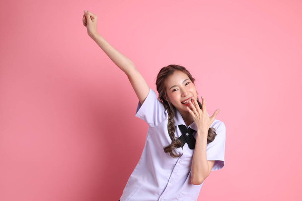Азиатка в тайской студенческой форме, стоящая на розовом фоне. - Фото, изображение