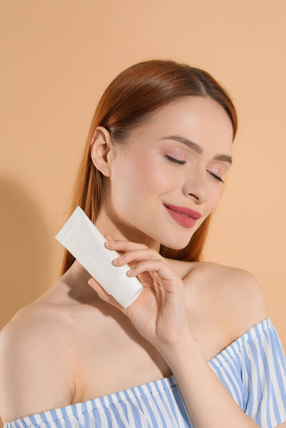 Beautiful young woman holding sun protection cream on beige background - Фото, зображення