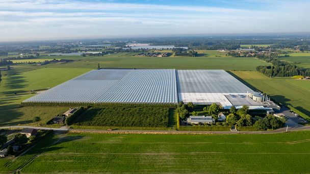 Een beklijvende luchtfoto die de geavanceerde wereld van de landbouw laat zien, met moderne industriële kassen die prominent staan te midden van uitgestrekte en weelderige landbouwvelden. Dit opvallende beeld vangt - Foto, afbeelding