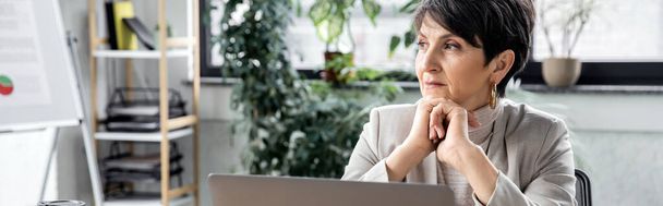 experiente, mulher de negócios pensativa olhando para longe perto do laptop no escritório, tomada de decisão, banner - Foto, Imagem