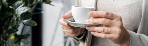 vista recortada de empresario de mediana edad con taza de café de pie en la oficina, pancarta - Foto, Imagen