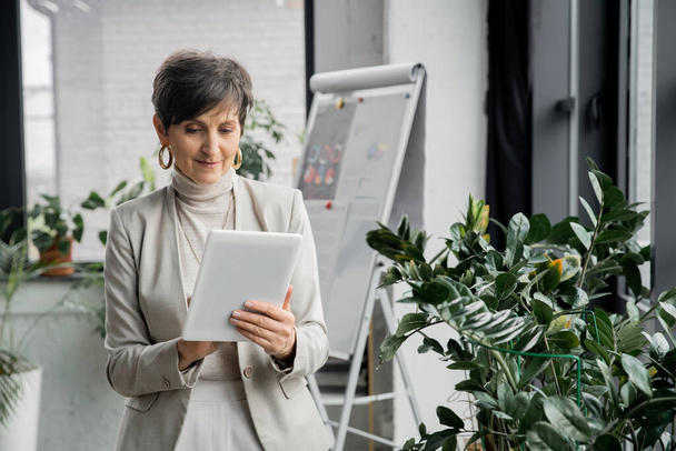 selbstbewusste Geschäftsfrau mittleren Alters mit digitalem Tablet im modernen Büro, Geschäftsplanung - Foto, Bild