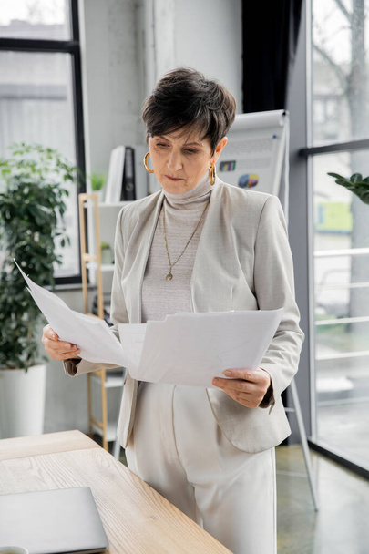 seriöse Frau, Führungskraft, die am Arbeitsplatz im Büro steht und Papiere betrachtet - Foto, Bild