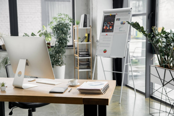 modern iroda, flip chart, grafikonok, íróasztal, számítógép monitor, notebook, dokumentumok, kávéscsésze - Fotó, kép