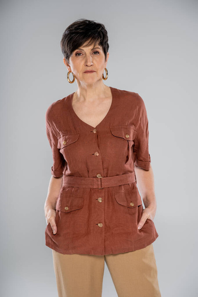 moda de otoño tendencia, morena mujer madura en chaqueta de lino marrón mirando a la cámara en gris - Foto, Imagen