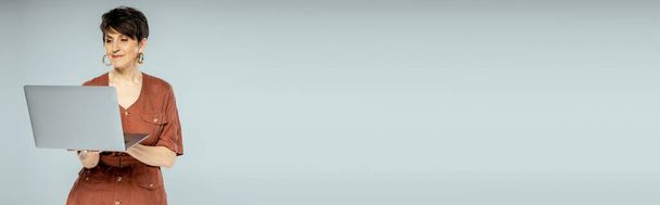 brunetta donna d'affari in giacca marrone utilizzando il computer portatile su grigio, moda autunno, look elegante, banner - Foto, immagini