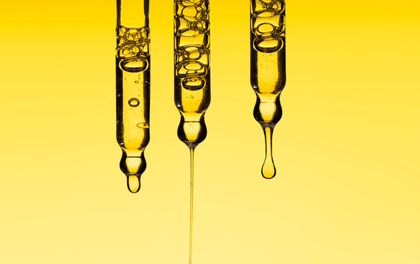 Set pipette serum drop with clear liquid oil, hyaluronic or Aha Bha acids on a yellow isolated background. Textured swatch skincare. Laboratory cosmetics - Photo, Image