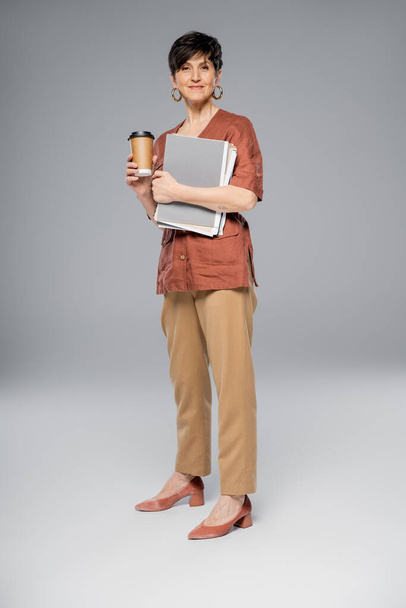 mujer de negocios de mediana edad con documentos, bebida para llevar en gris, aspecto elegante otoño, longitud completa - Foto, imagen