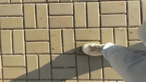 Una donna in jeans leggeri e scarpe da ginnastica bianche cammina su lastre di pavimentazione, vista dall'alto, gambe close-up, passi. - Filmati, video