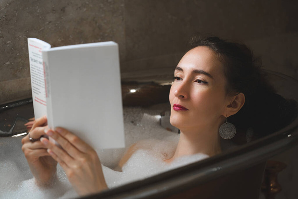 красивая сексуальная девушка в ванне с пеной читает книгу - Фото, изображение