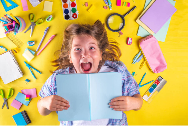 Cute emocjonalna dziewczyna gotowa do powrotu do szkoły z różnych materiałów szkolnych, akcesoria edukacyjne na jasnożółtym tle - Zdjęcie, obraz