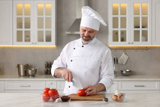 Professional chef cutting tomatoes at white marble table indoors - Фото, зображення