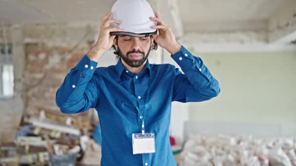 Young hispanic man architect wearing hardhat smiling at construction site - Footage, Video