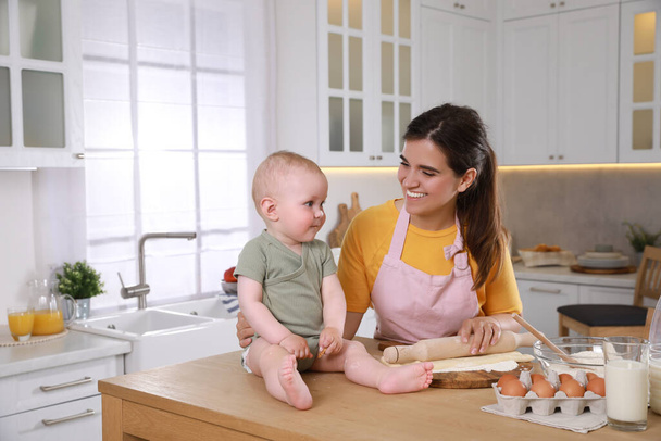 Happy young woman and her cute little baby cooking together in kitchen - Фото, изображение
