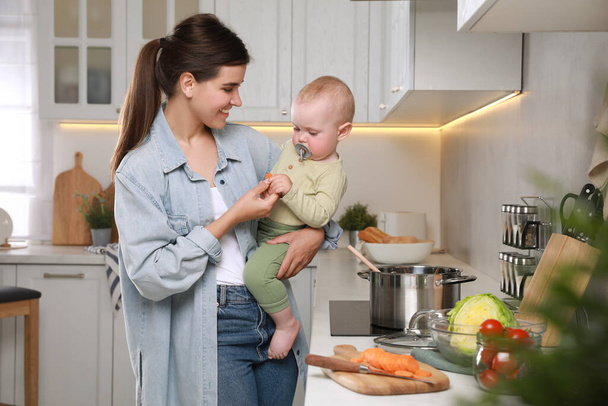 Happy young woman and her cute little baby cooking together in kitchen - Foto, afbeelding