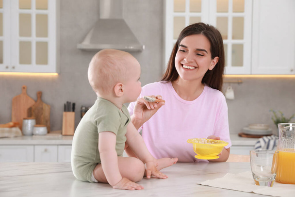 Happy young woman feeding her cute little baby at table in kitchen - Photo, Image