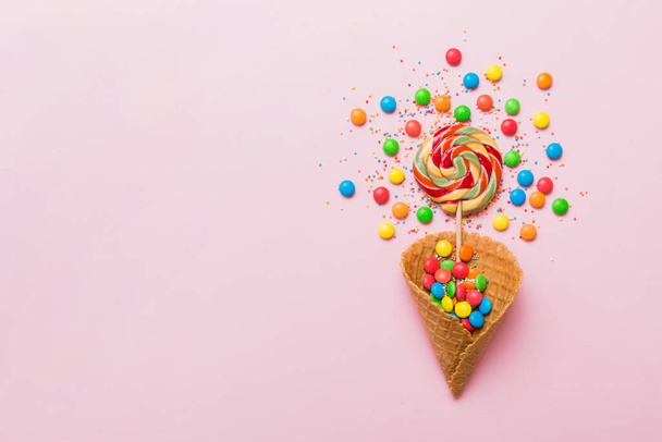 waffle cone full of assorted traditional candies falling out on colored background with copy space. Happy Holidays sale concept. - Photo, image