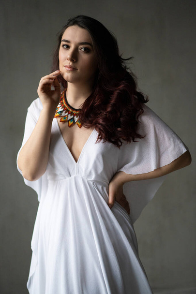 красива молода дівчина в білій сукні з намистом для прикрас ручної роботи навколо шиї - Фото, зображення