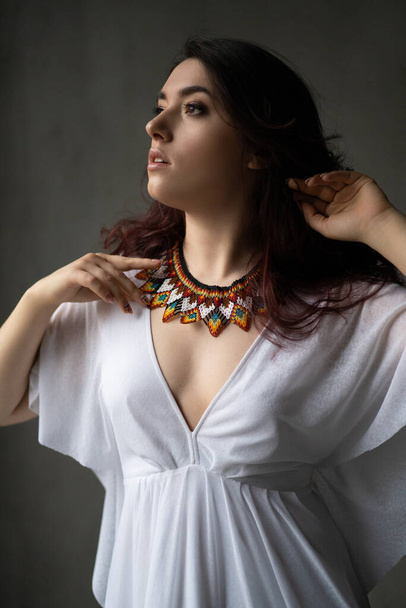 una hermosa joven en un vestido blanco con un collar de joyas hechas a mano alrededor de su cuello - Foto, Imagen