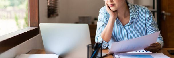 Nahaufnahme einer Geschäftsfrau, die Geschäftsdokument hält, während sie Strategie denkt und Daten auf dem Laptop liest. - Foto, Bild