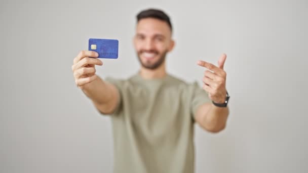 Fiatal spanyol férfi kezében hitelkártya csinál hüvelykujj fel gesztus mosolyogva elszigetelt fehér háttér - Felvétel, videó