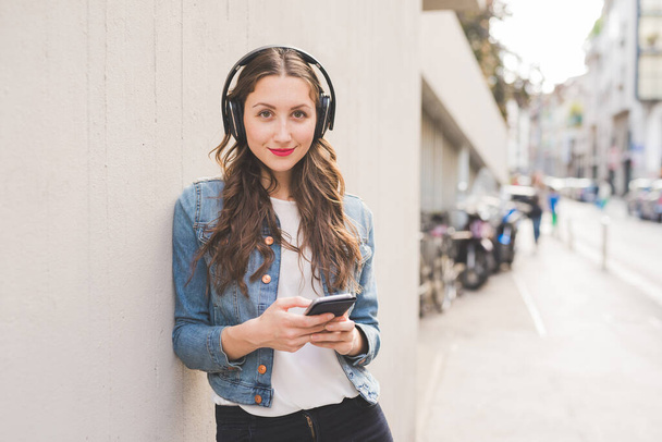 若い女性ミレニアル世代は,屋外でスマートフォンを使用して音楽を聞く - 写真・画像