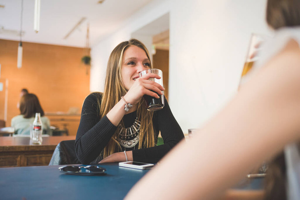 Twee jonge vrouwen zitten binnen bar kletsen en praten frisdrank te drinken - Foto, afbeelding