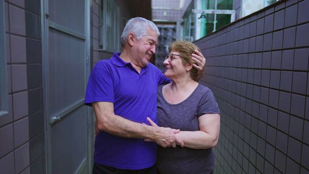 Muotokuva vanhemmasta pariskunnasta hymyilemässä yhdessä rakastavassa syleilyssä takapihan kotikäytävällä. Vanhukset naimisissa aviomies ja vaimo hellä hetki vanhuudessa, pitkäaikainen avioliitto - Valokuva, kuva