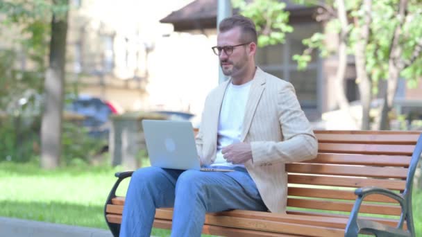 Μεσήλικας άντρας που χρησιμοποιεί φορητό υπολογιστή με πόνο στην πλάτη ενώ κάθεται σε εξωτερικούς χώρους - Πλάνα, βίντεο