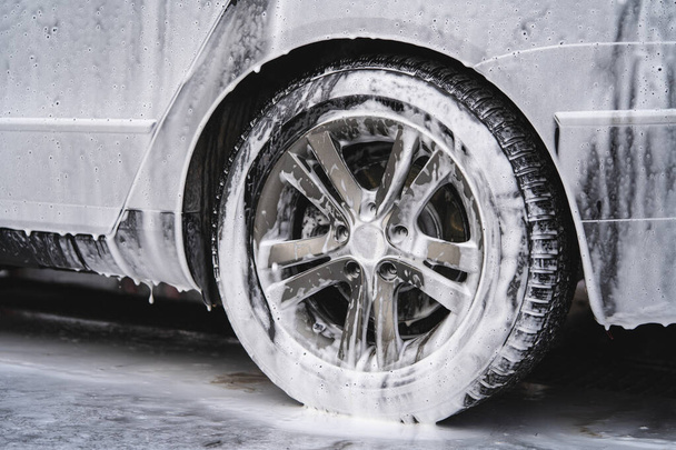 το αυτοκίνητο στο πλυντήριο αυτοκινήτων καλύπτεται με αφρό, πλένεται υπό πίεση με ρεύμα νερού - Φωτογραφία, εικόνα