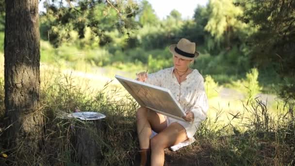 Μια γυναίκα καλλιτέχνης ζωγραφίζει μια εικόνα κατά τη διάρκεια της δύσης. Καλλιτέχνης, τέχνη προς πώληση, έμπνευση στη φύση. - Πλάνα, βίντεο