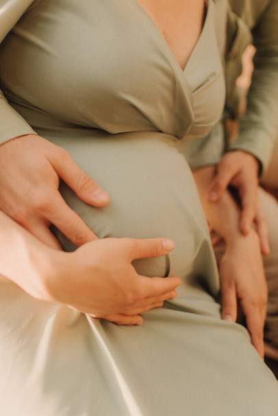 Großaufnahme auf dem Bauch einer schwangeren Frau, die ein langes grünes Kleid trägt. Neues Lebenskonzept. Kein verschwommener Fokus und Rauscheffekt - Foto, Bild