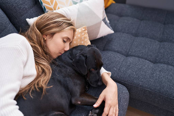 Young blonde woman lying on sofa sleeping with dog at home - Photo, Image