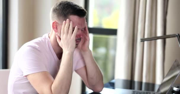 Frustrated freelancer sitting at home in front of laptop and closing eyes. Man overworked by computer feels sudden headache - Filmmaterial, Video