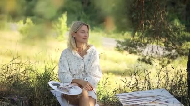 Een vrouw schildert op een doek in het bos. Gelukkige kunstenaar buiten. Helder zonlicht in het frame. - Video