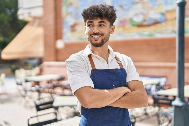Young arab man waiter standing with arms crossed gesture at restaurant - Fotó, kép