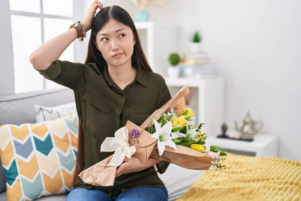 Китайська молода жінка, що тримає букет білих квітів, плутає і задається питанням. непевне з сумнівом, мислення з рукою на голову. пенсійна концепція.  - Фото, зображення