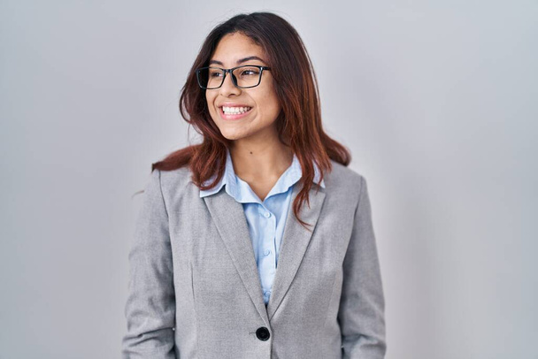 Hispanische junge Geschäftsfrau mit Brille, die mit einem Lächeln im Gesicht und natürlichem Gesichtsausdruck zur Seite schaut. Lachen selbstbewusst.  - Foto, Bild