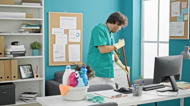 Hombre hispano joven limpiador profesional piso de limpieza en la oficina - Foto, Imagen