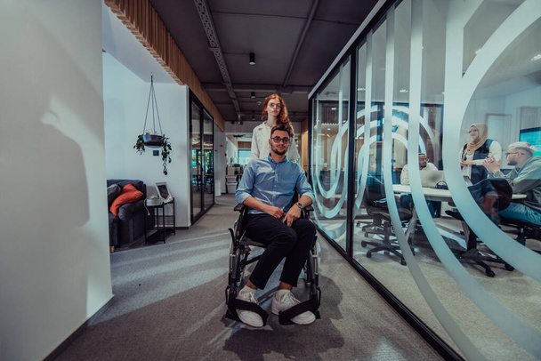 Young business colleagues, collaborative business colleagues, including a person in a wheelchair, walk past a modern glass office corridor, illustrating diversity, teamwork and empowerment in the - Foto, Imagen